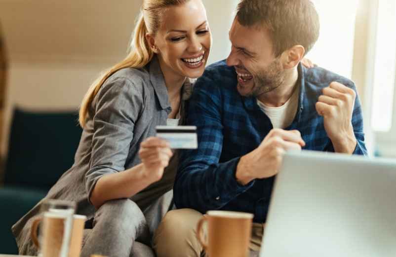 Happy young couple holding house keys standing in front of their new modern home with big smiles